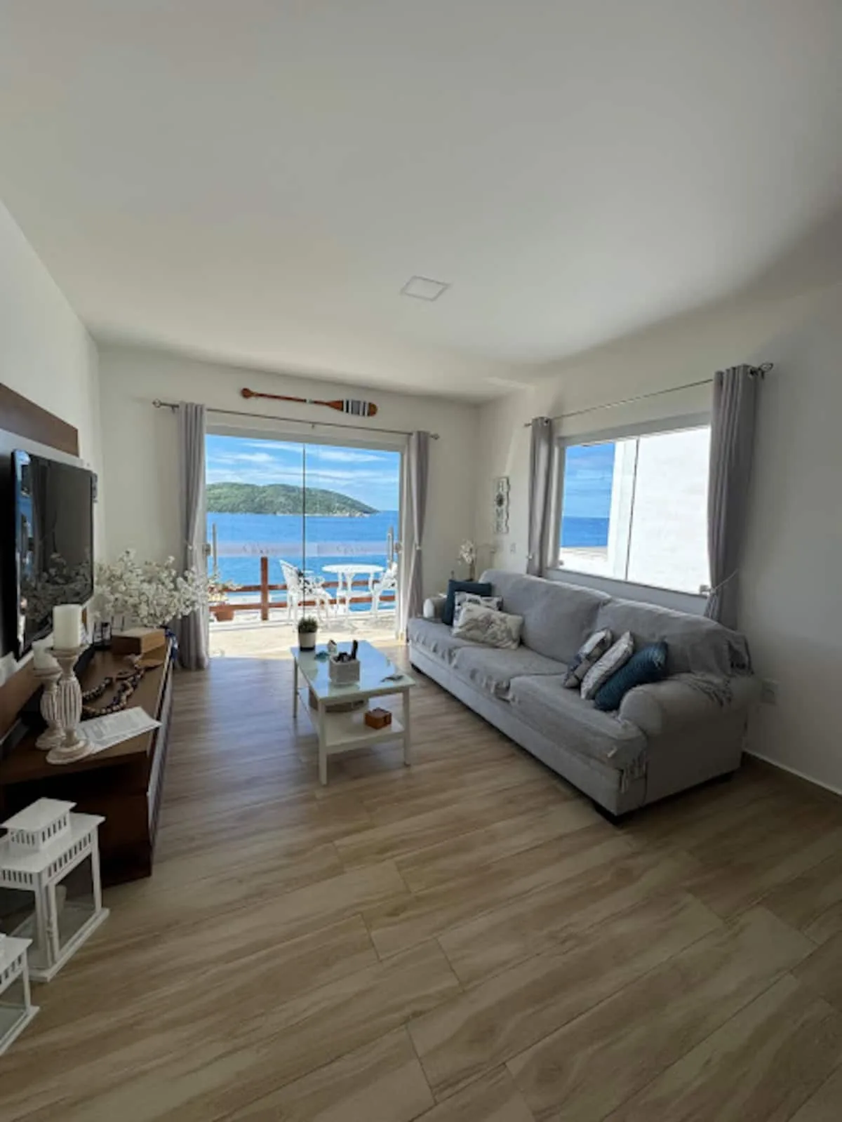 Sala de estar com sofá, Smart TV e porta de vidro para a vista do mar